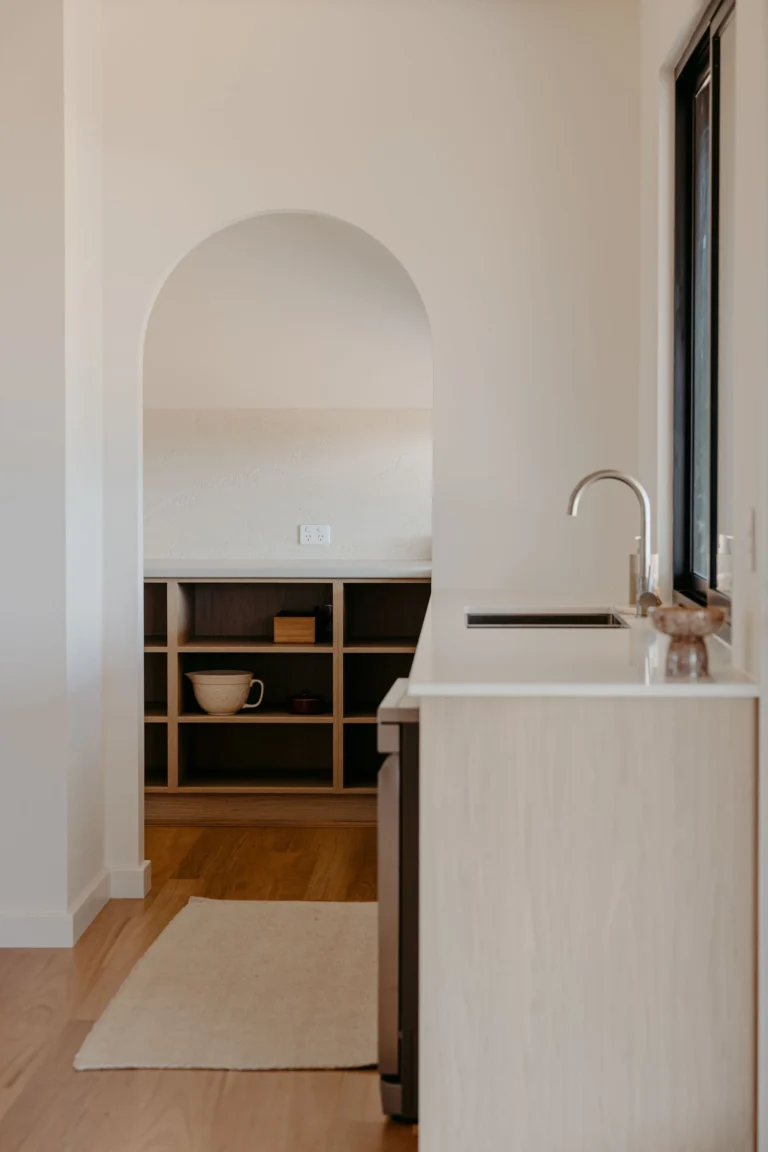 View past the kitchen sink to the arched butler's pantry, with open shelving and a jute runner on the timber floor