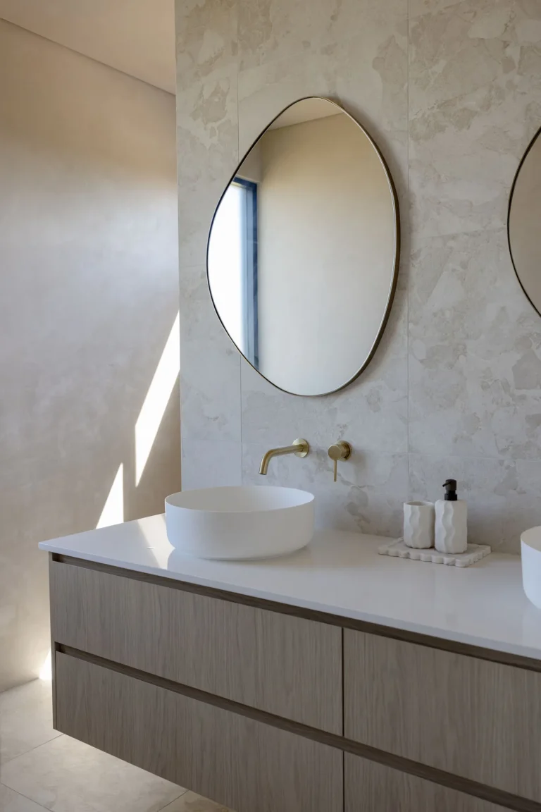 Ensuite vanity with a round white vessel basin and brushed brass tapware, afternoon light falling across the rendered wall