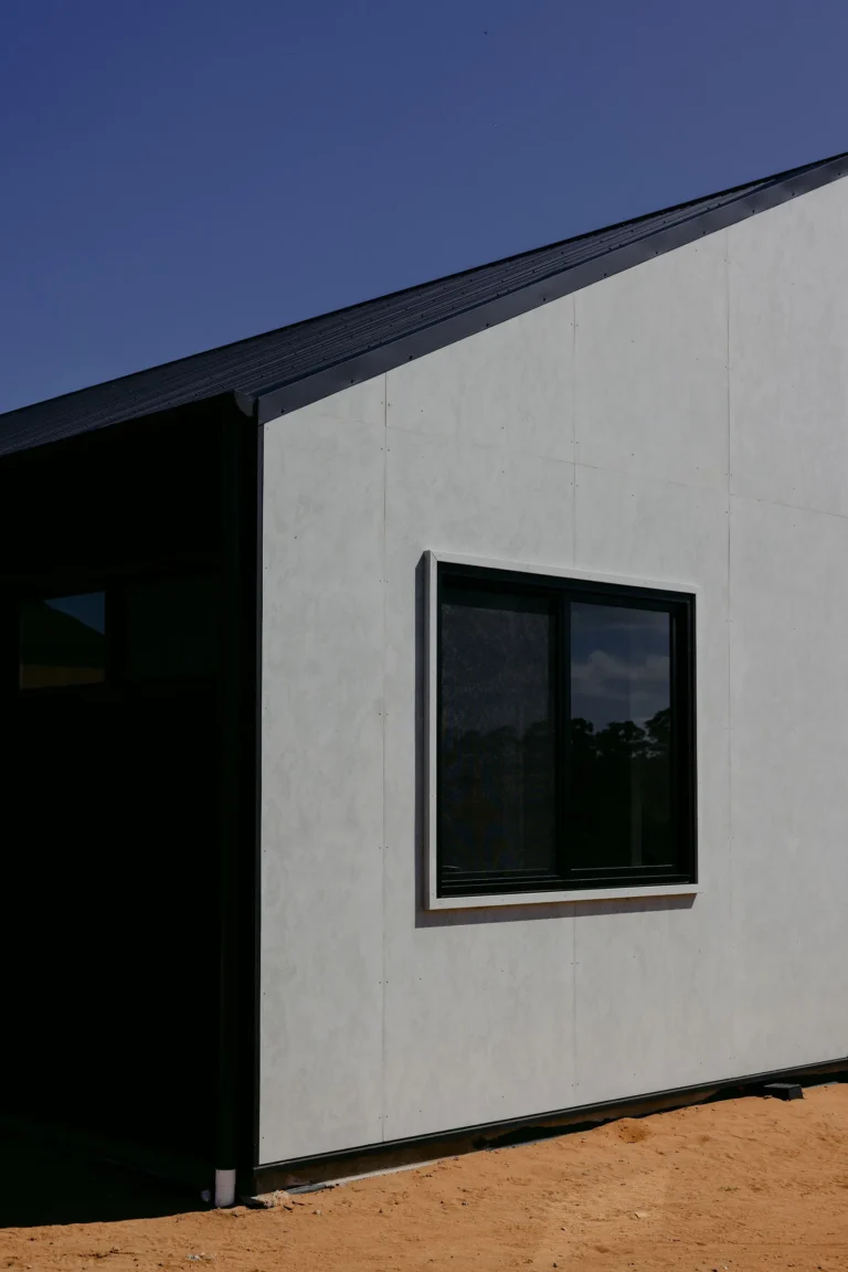 Fibre cement panel cladding with a black-framed window and dark roofline against a deep blue sky