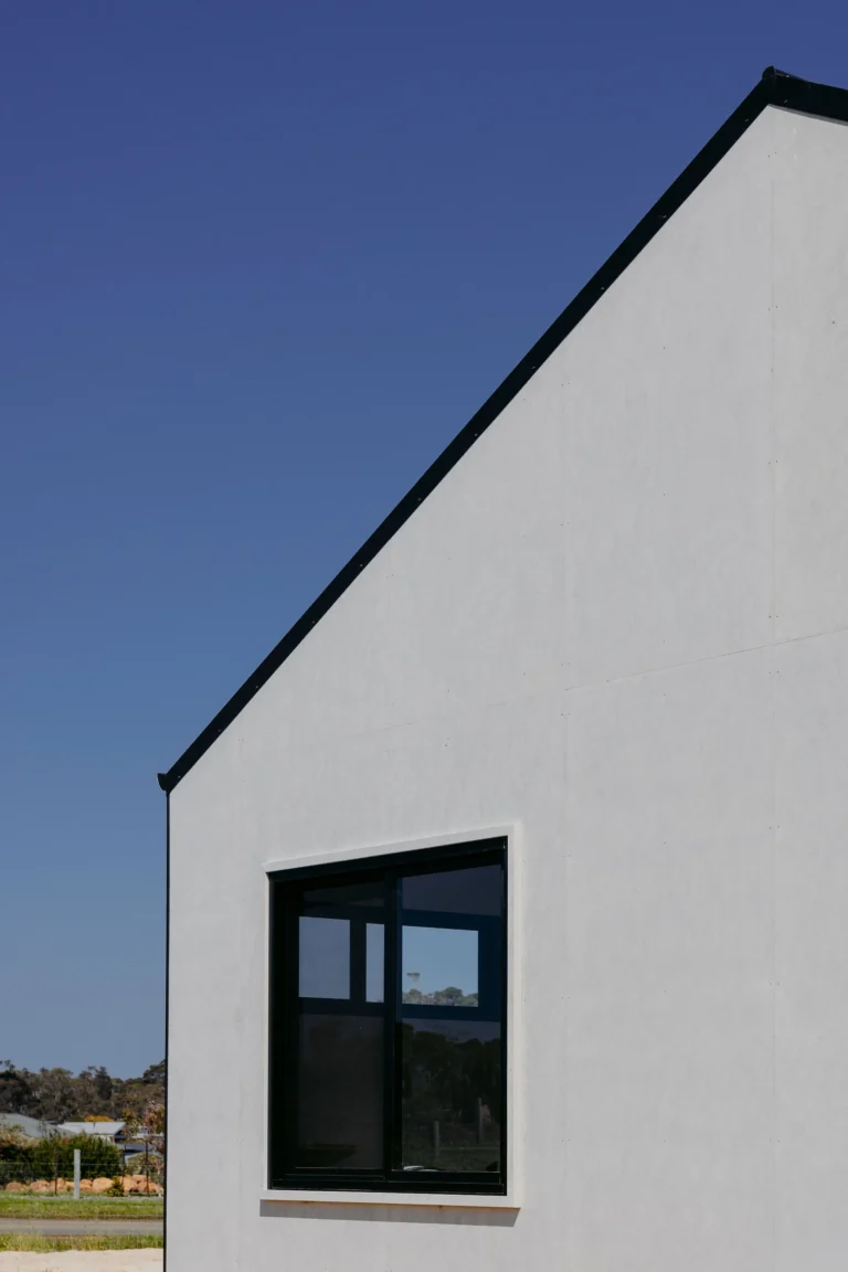 Steep gable of the Felling Karridale home in fibre cement cladding, with a black-framed window and bushland beyond