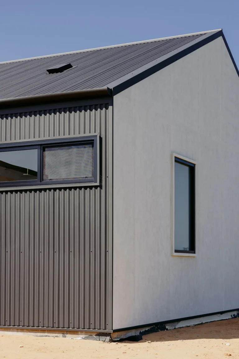 Corner of the home where dark corrugated cladding meets fibre cement panels, with black-framed windows and a corrugated roof