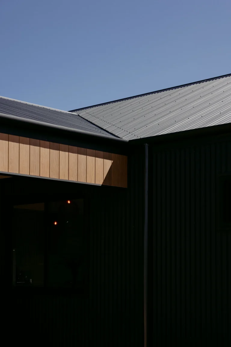 Intersecting corrugated rooflines above a timber-look clad fascia and dark corrugated walls in full sun