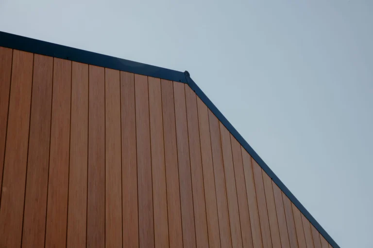 Vertical timber-look cladding on a gable end with a dark metal roof edge against a pale sky