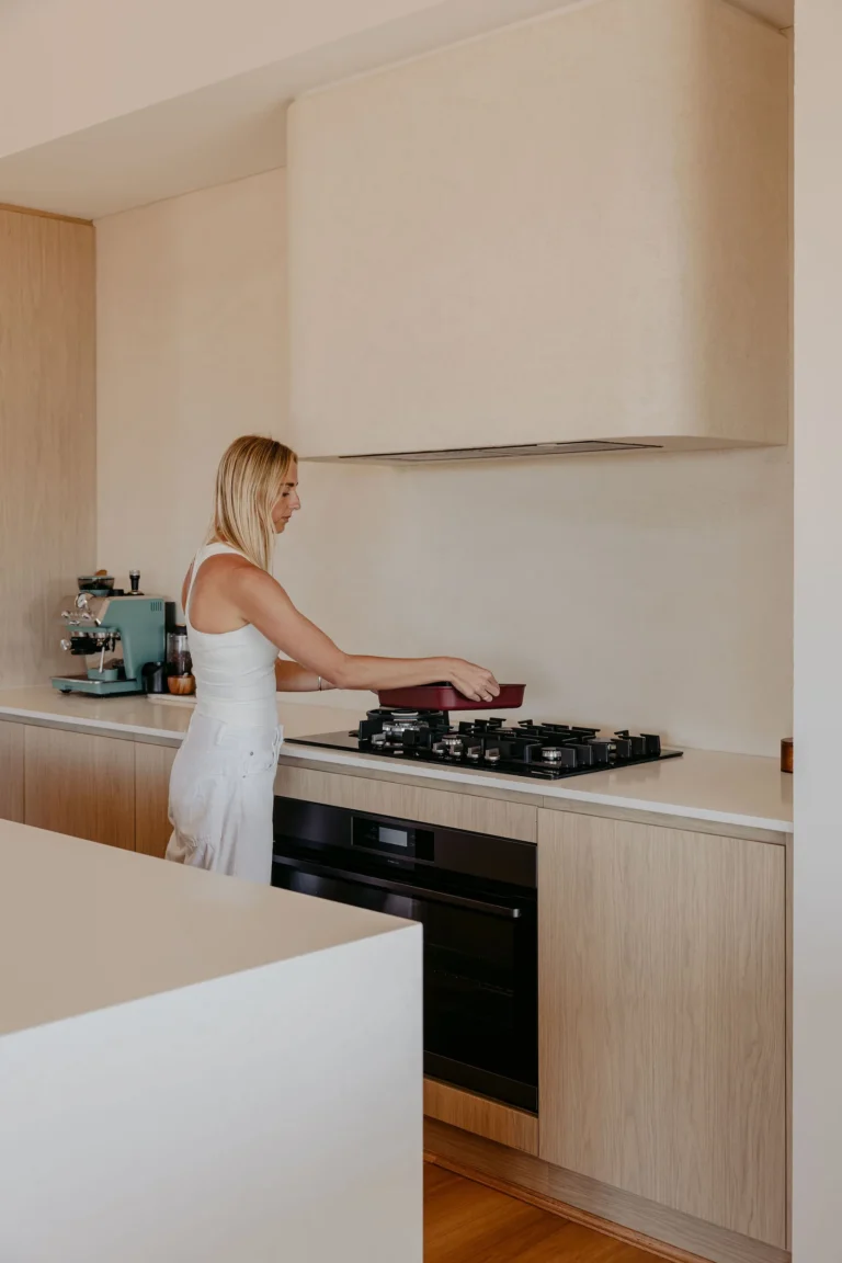 Gas cooktop and black wall oven set into oak-look cabinetry beneath a curved rendered rangehood in the Felling Karridale kitchen