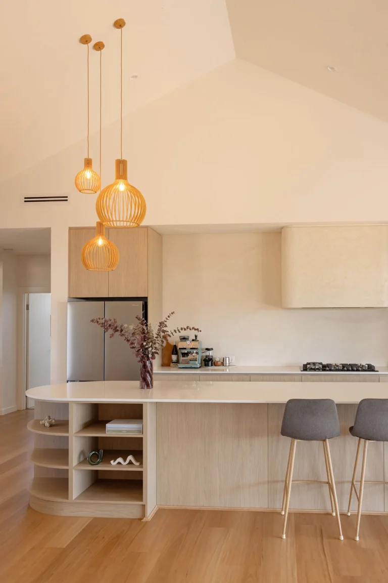 Three timber cage pendants hanging from the raked ceiling over the kitchen island, with oak-look cabinetry and a textured rendered rangehood behind