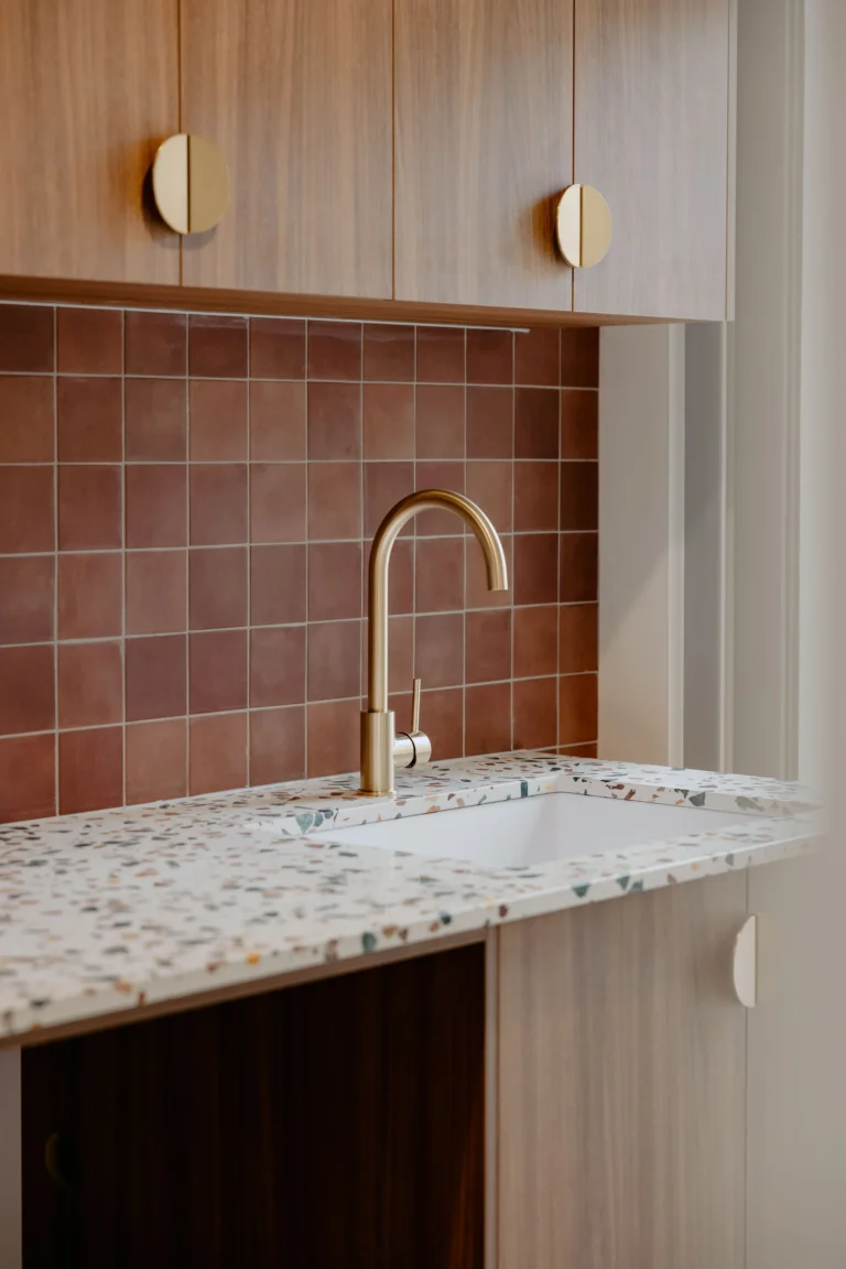 Laundry with a terracotta tiled splashback, terrazzo benchtop, brass tap and timber cabinetry