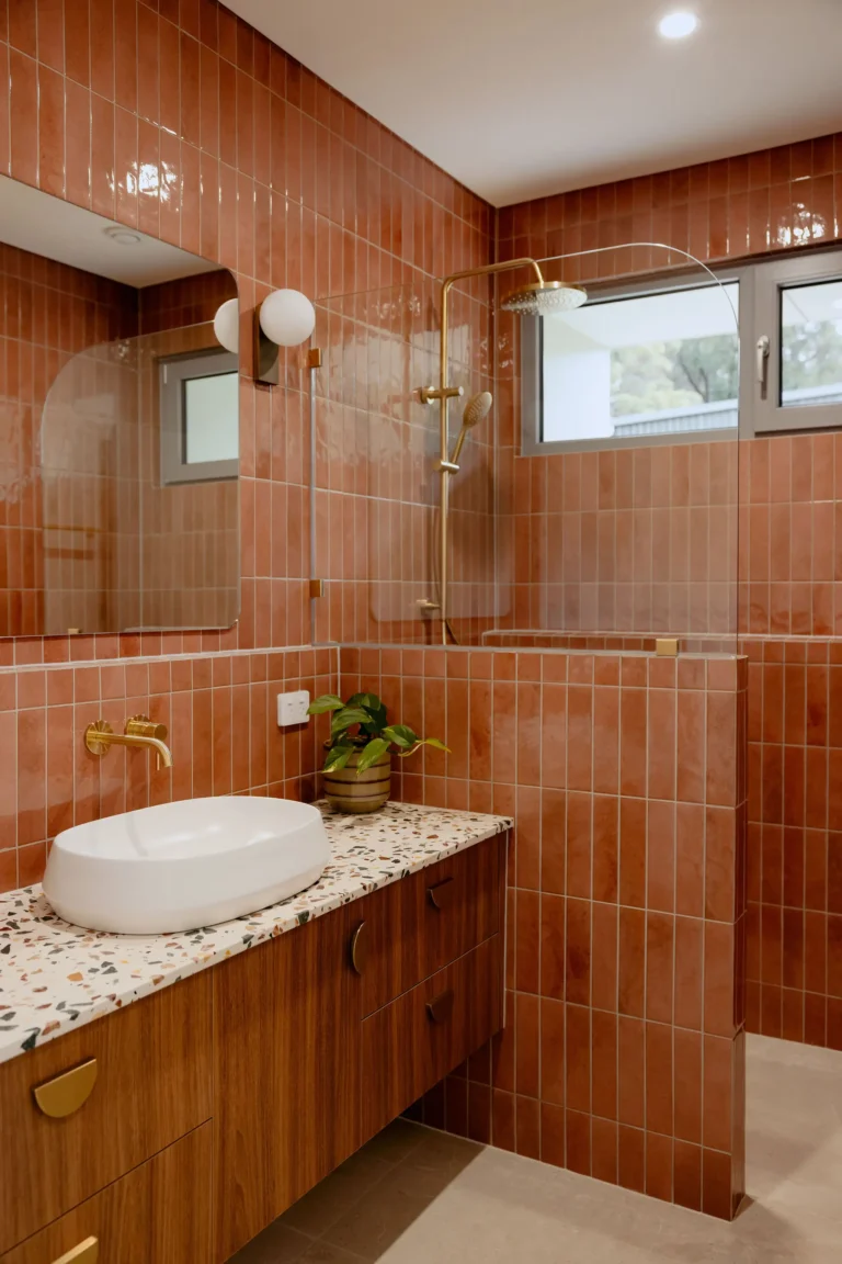 Bathroom with terracotta tiled walls, a terrazzo-topped timber vanity, brass tapware and walk-in shower