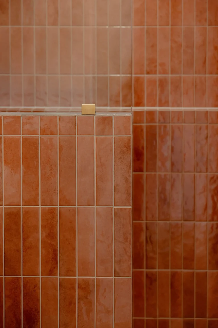 Detail of terracotta vertical wall tiles with a brushed brass tile trim