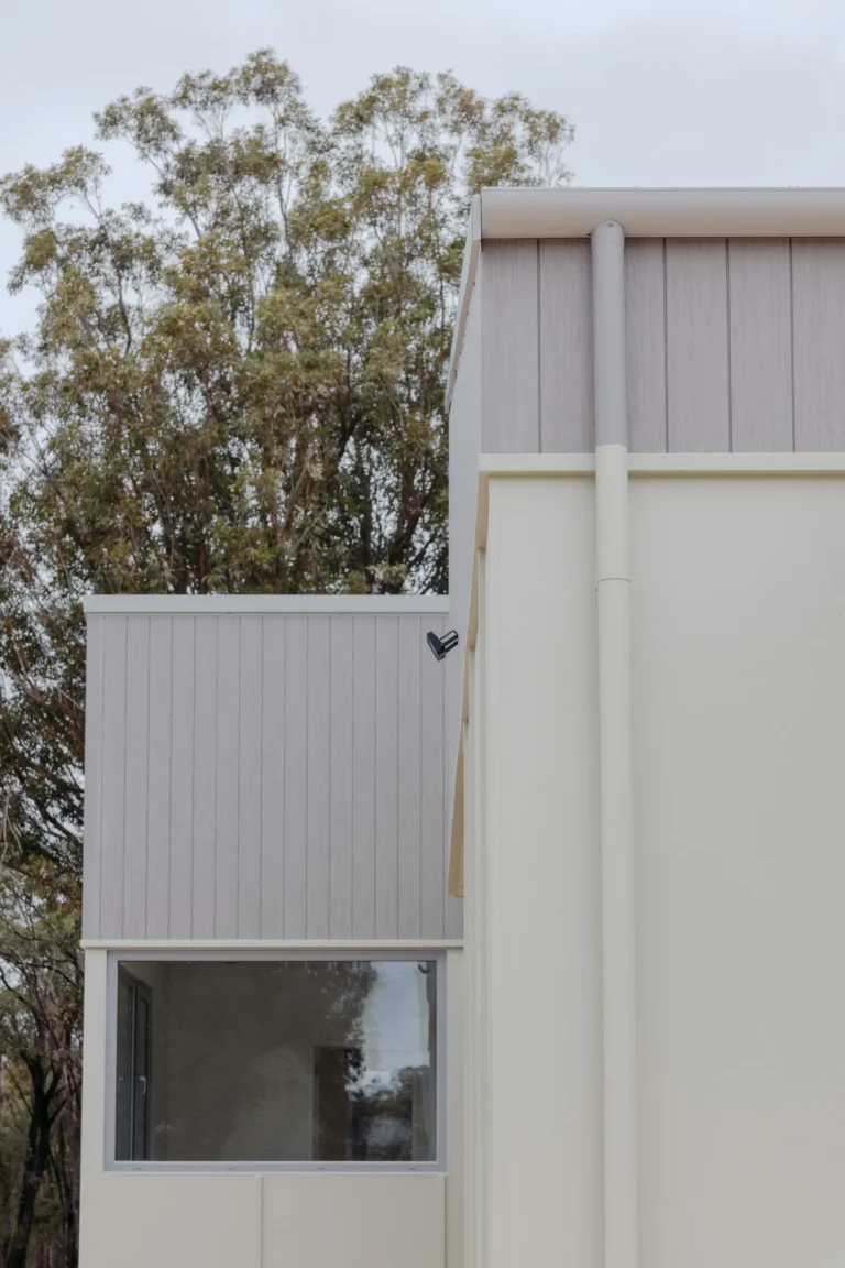 Exterior cladding detail with vertical boards and a rounded parapet against native trees