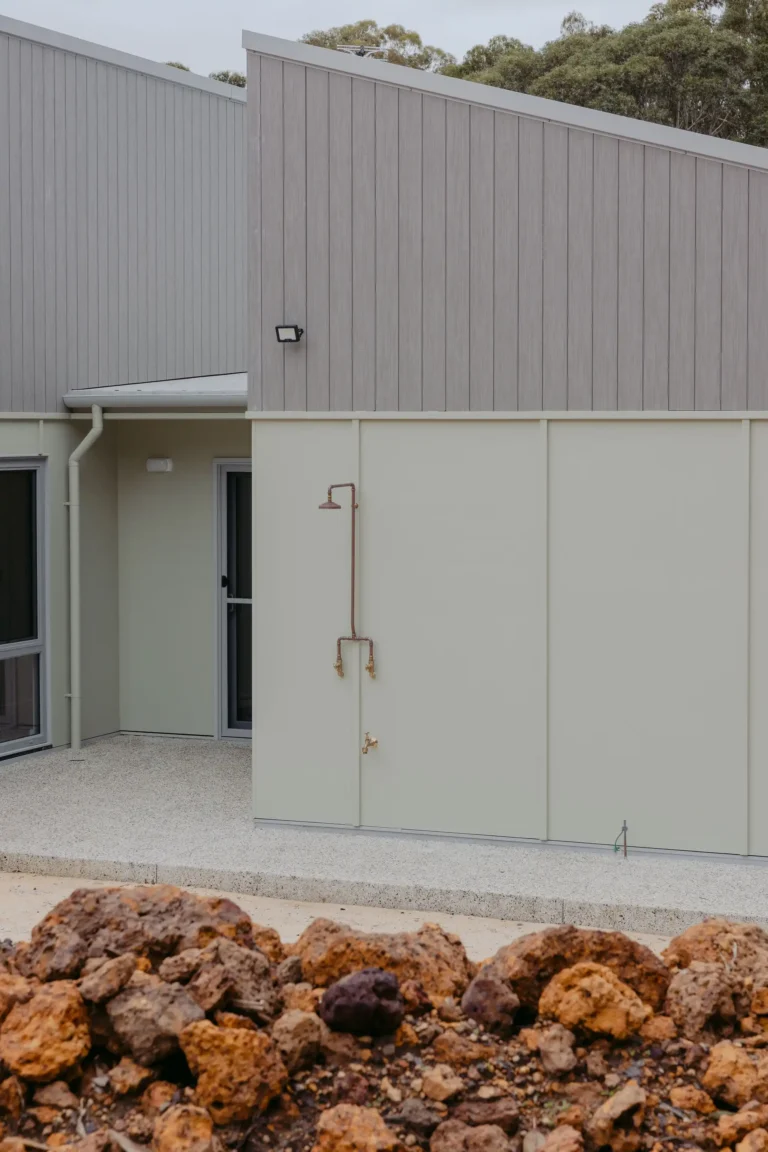 Exterior wall with a copper outdoor shower beside the entry door and laterite rock garden