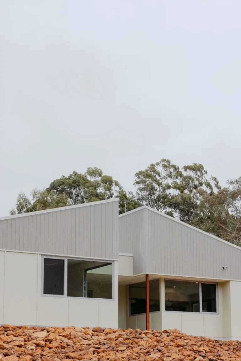 Exterior elevation with dual pitched roofs and picture windows above a laterite rock garden