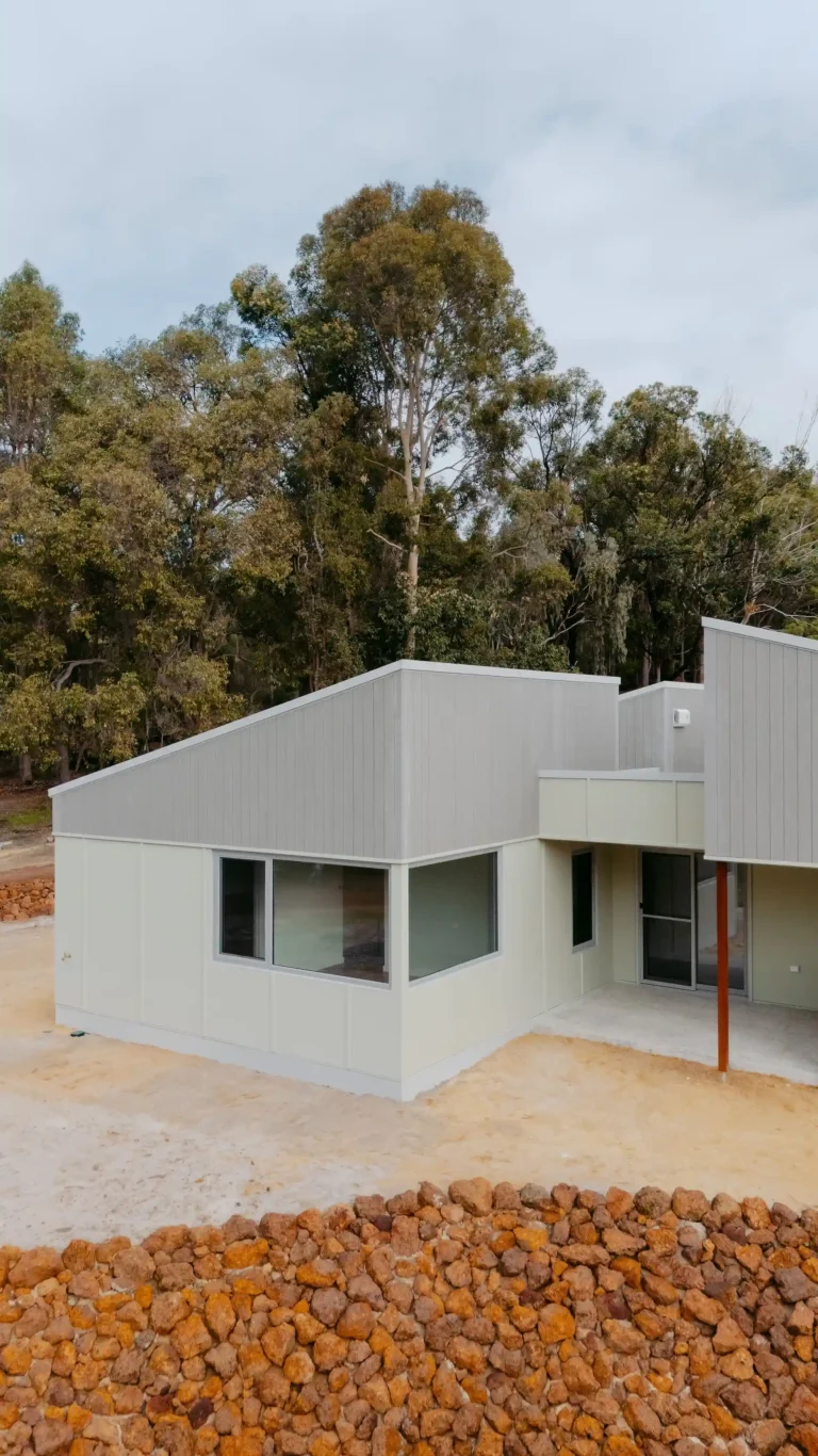 Exterior corner of the Indianic Homes Woodbridge house with wraparound windows and courtyard among gum trees