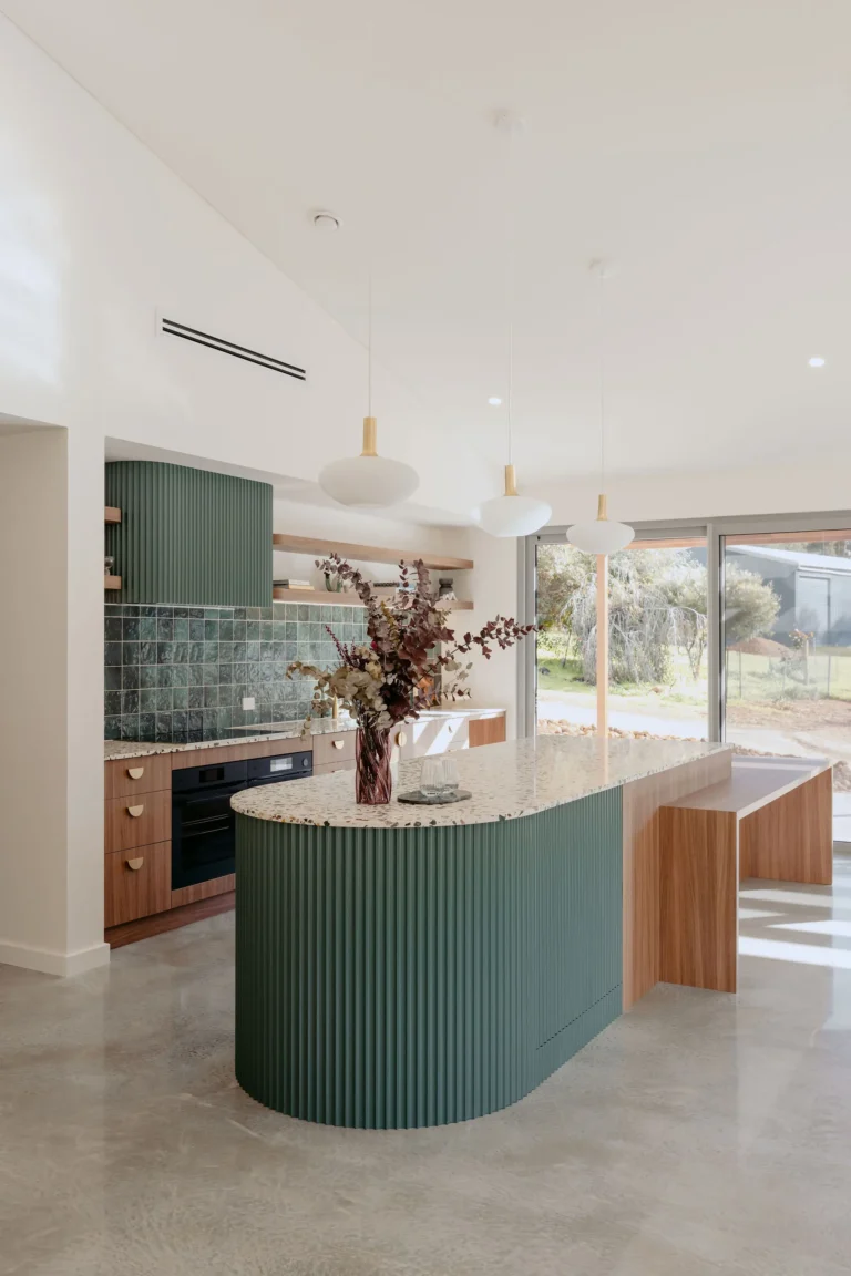 Kitchen with a curved sage-green fluted island, terrazzo benchtop and pendant lights beside floor-to-ceiling windows
