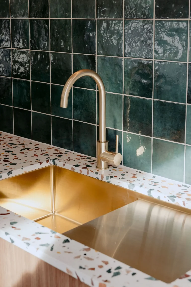 Brushed brass undermount sink set into a terrazzo benchtop against a green glazed tile splashback