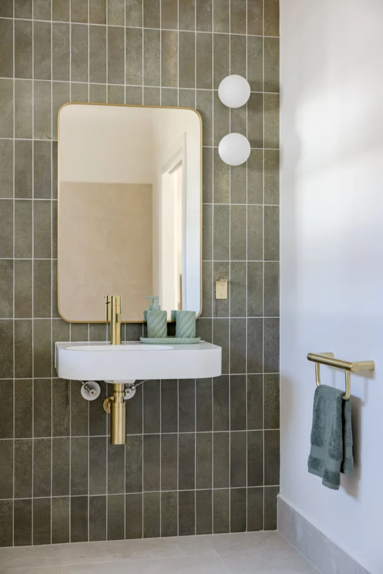 Accessible bathroom vanity with wall-hung basin, brushed brass tapware and brass-framed mirror against sage green tiles