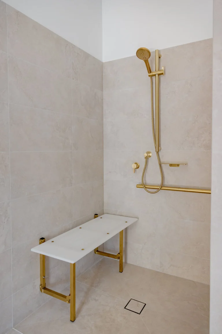 Step-free accessible shower with brushed brass hand shower, grab rail and white shower bench