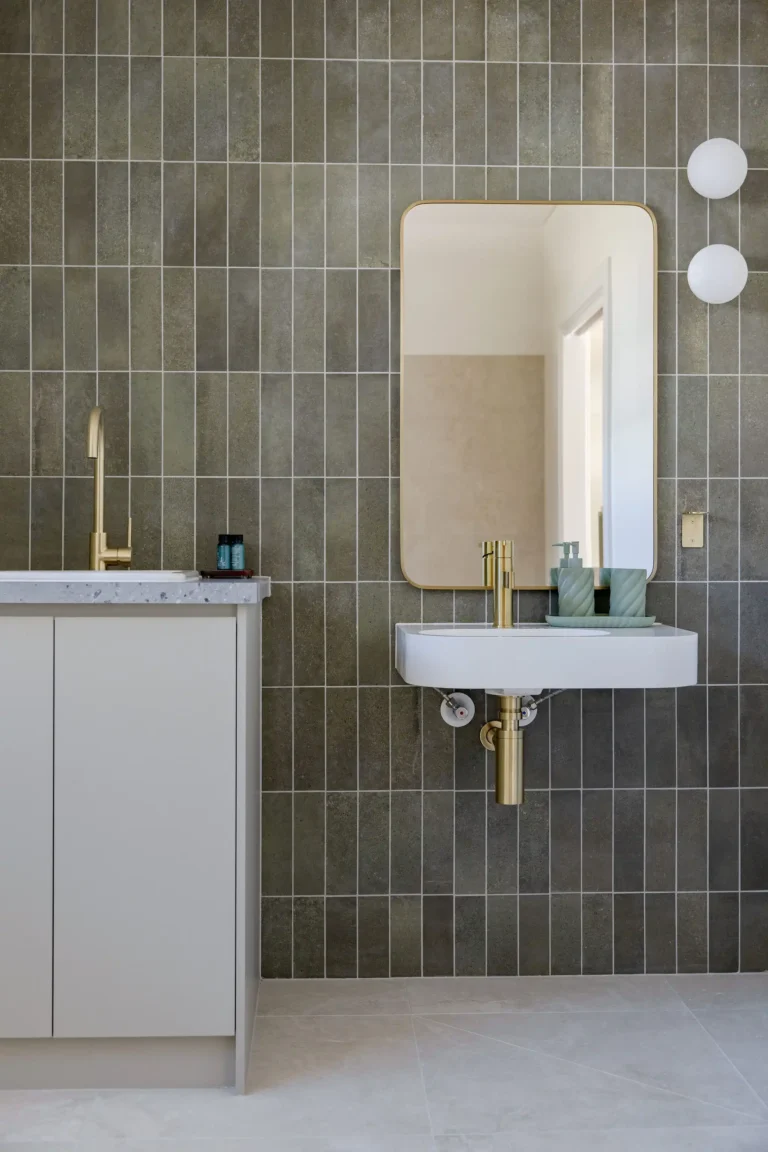 Bathroom with wall-hung basin beside a stone-topped cabinet, brushed brass tapware and sage green vertical tiles