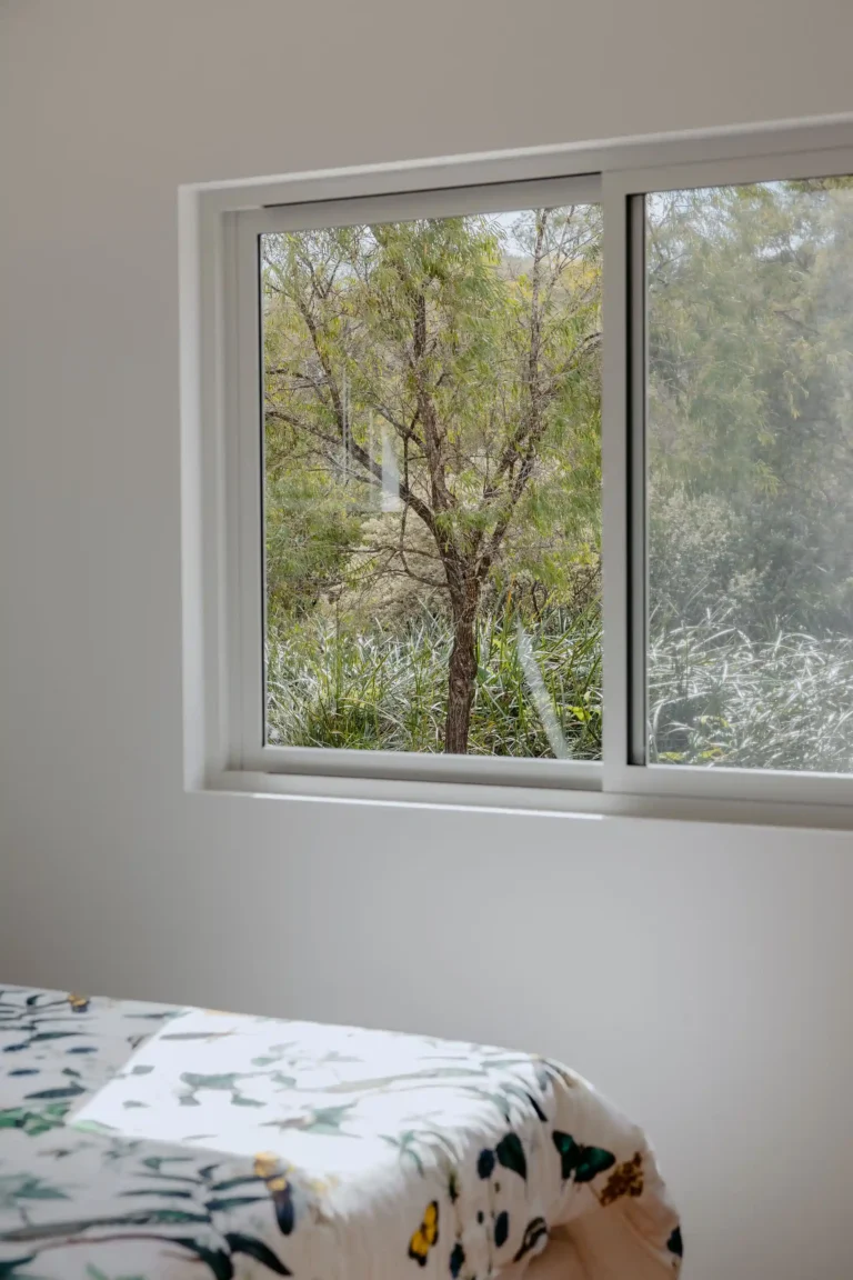 Bedroom window framing native bushland, with a botanical print quilt on the bed