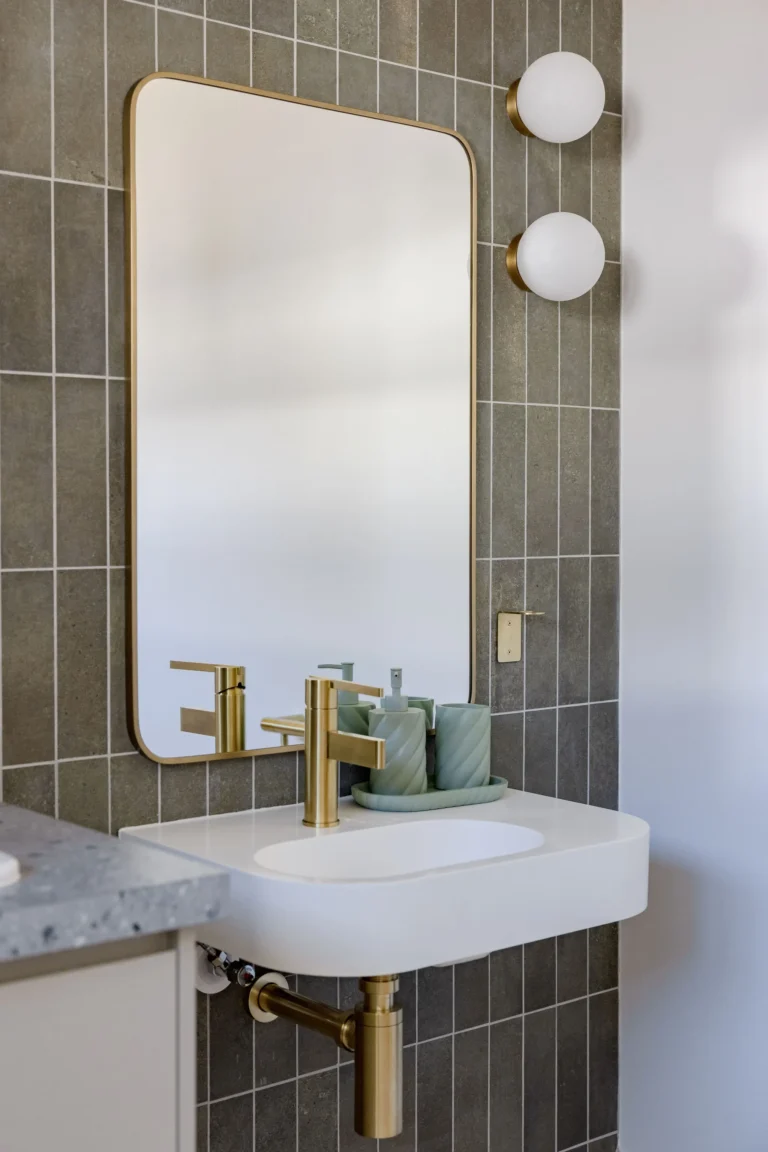 Close-up of a wall-hung basin with brushed brass mixer, brass-framed mirror and globe wall lights