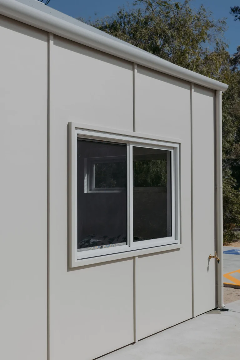 Exterior detail of a sliding window set into the cabin's pale panelled cladding