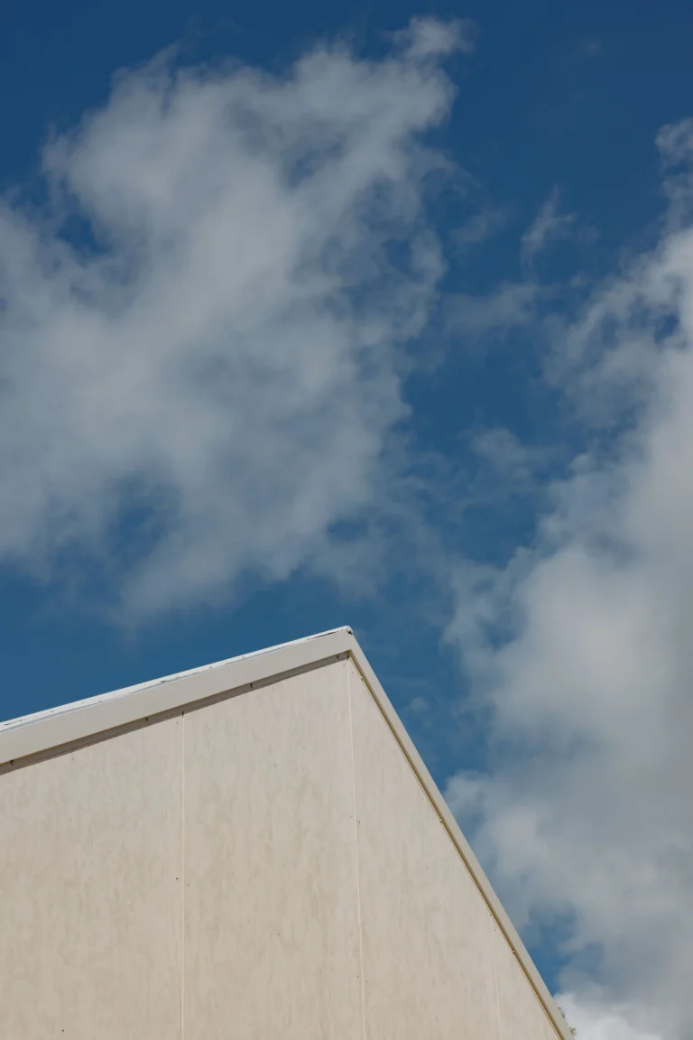 Detail of the cabin's gable roofline against a blue sky and clouds