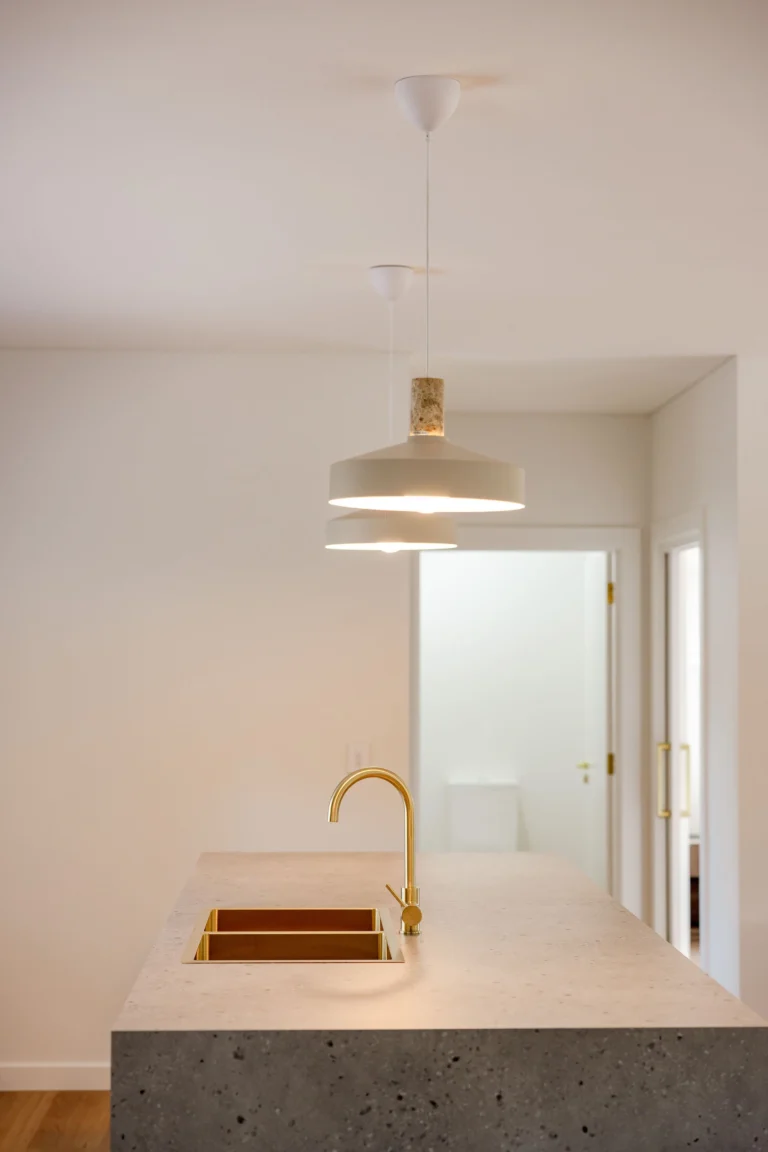 Brass gooseneck tap and sink set into the stone island bench beneath pendant lights