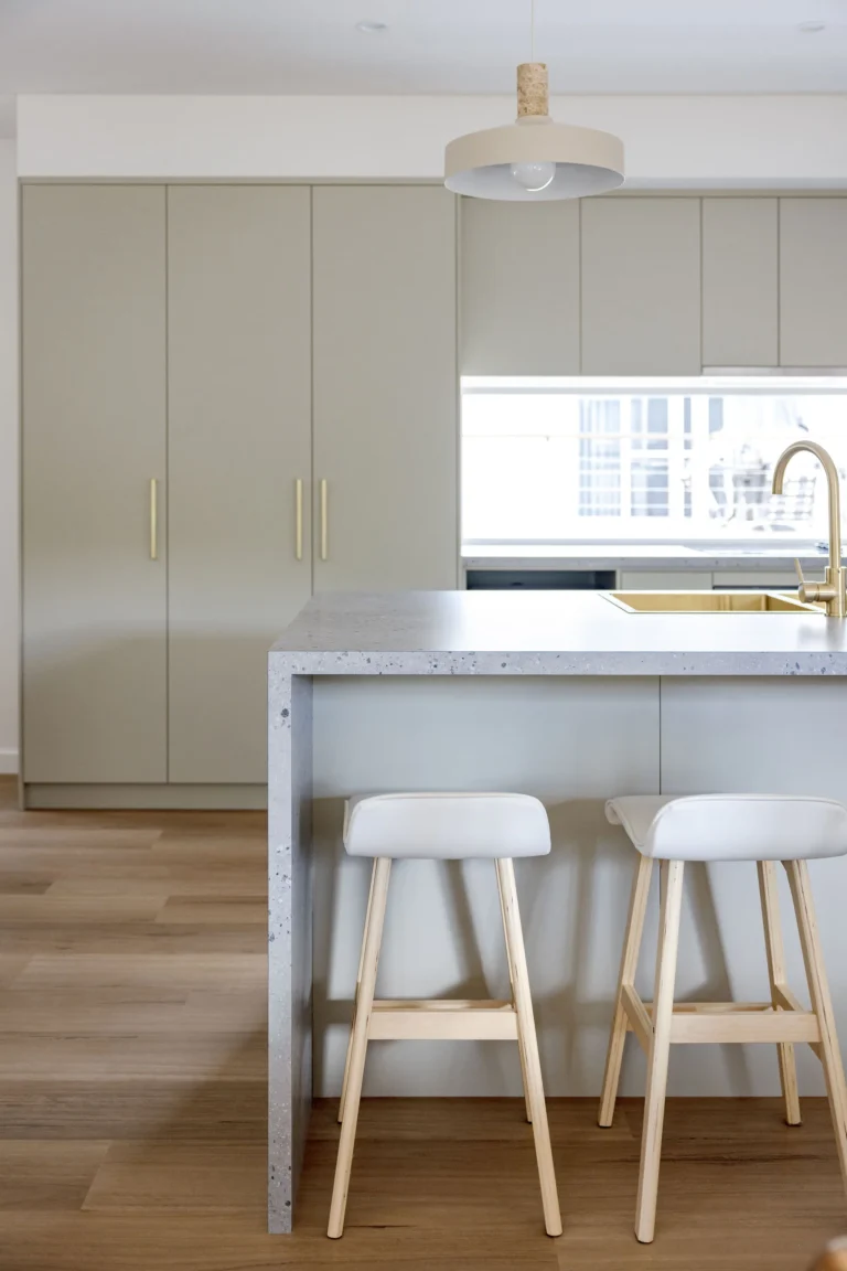 Kitchen island with speckled stone waterfall benchtop and white bar stools on timber legs