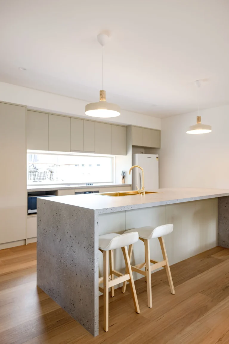 Kitchen with stone waterfall island, brass sink and tapware, sage cabinetry and pendant lights