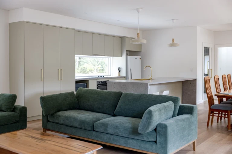 Open-plan living area with teal sofa and timber floors, flowing to the sage kitchen and dining area